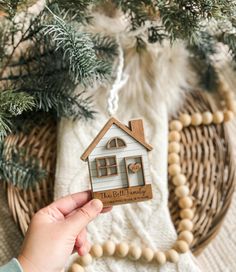 a hand holding a wooden house ornament in front of a christmas tree with ornaments around it