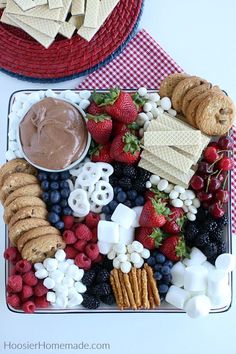 a platter filled with crackers, strawberries, raspberries, marshmallows and other snacks