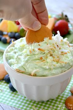 a person dipping something into a bowl with fruit on the table in the back ground