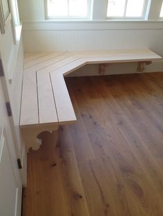 a wooden bench sitting on top of a hard wood floor next to a window in a room