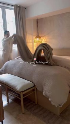 a man standing next to a bed with white sheets and pillows on top of it