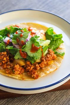 a taco with lettuce, sauce and other toppings on it sitting on a plate