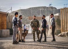 a group of men standing next to each other in front of a fenced area