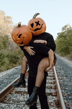 two people dressed up as jack and pumpkins hugging on train tracks with trees in the background