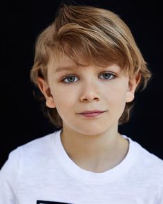 a young boy wearing a white t - shirt and looking at the camera with a serious look on his face