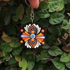 a hand holding a black, orange and blue flower shaped keychain in front of some green leaves