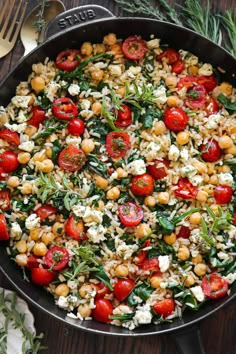 a skillet filled with tomatoes, chickpeas and spinach on top of a wooden table