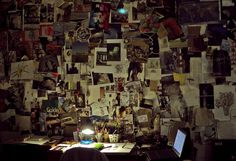 a person sitting at a desk in front of a wall covered with pictures and papers