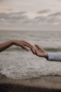 two hands reaching out towards each other near the ocean