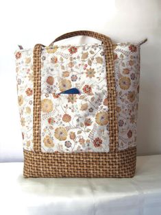 "This tote is constructed from a pretty cotton print of light brown wildflowers strewn on a cream background. The straps and bottom border, made from a basket weave cotton print. The slot pocket on one side of the exterior is just right for storing your cell phone but keeping it available for quick access. The two handles are 19\" long, with a 7\" drop. A recessed zipper closure at the top secures the contents.  It is fully lined with a light brown leaf batik and features three slot pockets for stashing those little items that are so easily lost in a big bag. Featuring quality construction, this bag is interfaced with a foam interfacing which provides structure and stability to the bag. The bottom of the bag is reinforced with a heavy fusible interfacing and has 4 metal feet to protect the Recessed Zipper, Fusible Interfacing, Wichita Ks, Big Bag, Cream Background, Big Bags, Tote Handbag, Basket Weave, Cotton Weaving