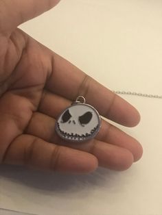 a hand holding a small pendant with a skull on it's face and eyes