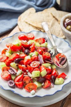 a white plate topped with cucumber salad next to a bowl of pita bread