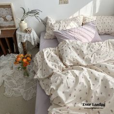 an unmade bed with white sheets and pink flowers on the table next to it