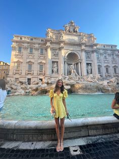 a woman standing next to a fountain in front of a building