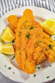 fried fish with lemon wedges and parsley on a white plate