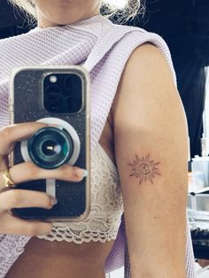 a woman taking a selfie with her camera and sun tattoo on her left arm