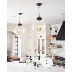 two lights hanging from the ceiling above a kitchen island with marble counter tops and white cabinets