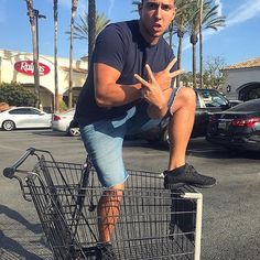 a man sitting on top of a shopping cart in a parking lot with palm trees