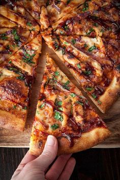 a person holding a slice of pizza in front of a wooden cutting board with several slices missing