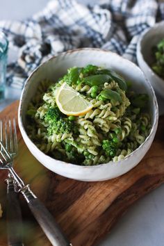 a bowl filled with pasta and broccoli on top of a wooden cutting board