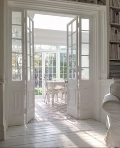 an open door leading into a room with white furniture and bookshelves on the wall