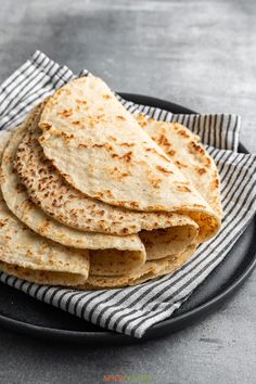 a black plate topped with tortillas on top of a white and black towel