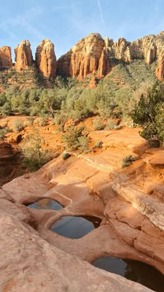 the rocks are red and brown with small pools in them near some trees, bushes and mountains