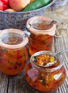 three jars filled with pickled vegetables on top of a wooden table next to a spoon