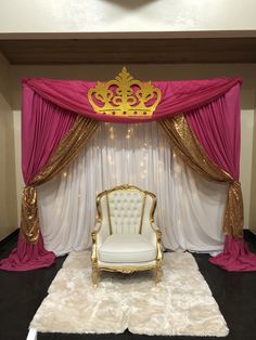 a white chair sitting in front of a red and gold stage drape with a crown on it