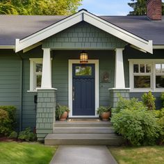 a blue front door on a gray house with white trim and columns, surrounded by greenery