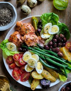 a white plate topped with lots of food next to bowls of eggs and olives