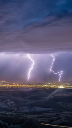 lightning strikes in the sky over a city at night with mountains and fields below it