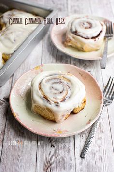 cinnamon roll with icing on a plate next to a knife and fork in the background