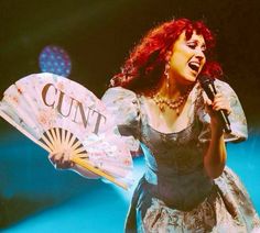 a woman with red hair is holding a fan and singing into a microphone on stage