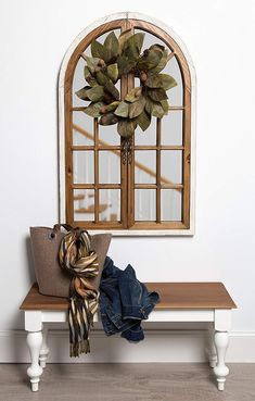 a wooden bench sitting under a window next to a purse and coat rack on top of a hard wood floor