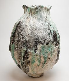 an old vase with green and black paint on it's sides, sitting against a white background