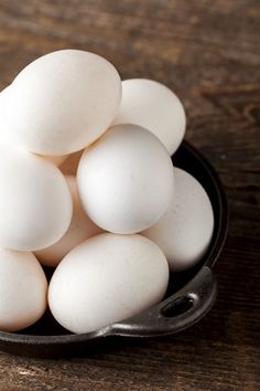 a black bowl filled with white eggs on top of a wooden table