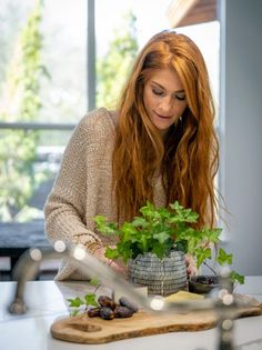 a woman looking at a potted plant on top of a kitchen counter next to a cutting board