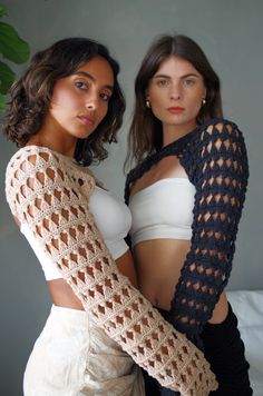 two beautiful women standing next to each other wearing crocheted arm warmers and scarves