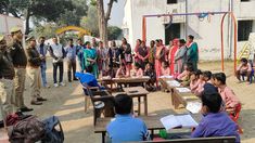 a group of people standing around each other in front of desks and chairs with papers on them