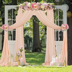 an outdoor wedding ceremony with pink drapes and flowers on the arch, decorated with candles