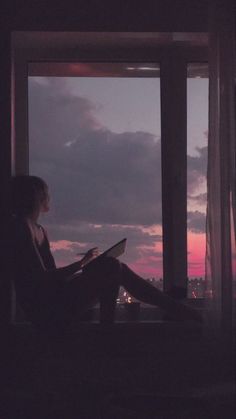 a woman sitting in front of a window reading a book