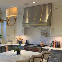 a kitchen with marble counter tops and stainless steel oven hood over the stove, surrounded by white chairs