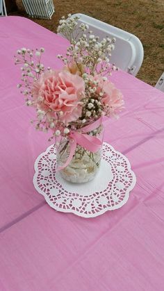 pink flowers in a vase on a doily at a table with chairs and tablescloths