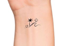 a small palm tree tattoo on the left side of the wrist, with a sun and two stars above it