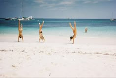 three people doing handstands on the beach with boats in the background