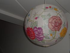 a paper lantern hanging from the ceiling with flowers painted on it and attached to a wall