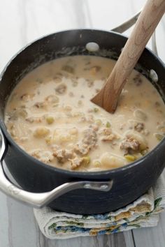 a pot filled with soup on top of a wooden table next to a napkin and spoon