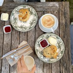 two plates with scones, jams and biscuits on them sitting on a wooden table