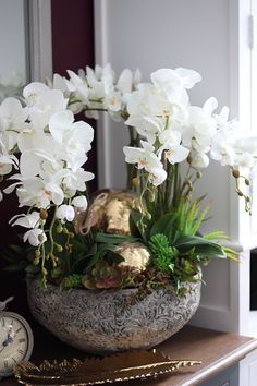 white flowers are in a bowl on a table next to a clock and other decorations